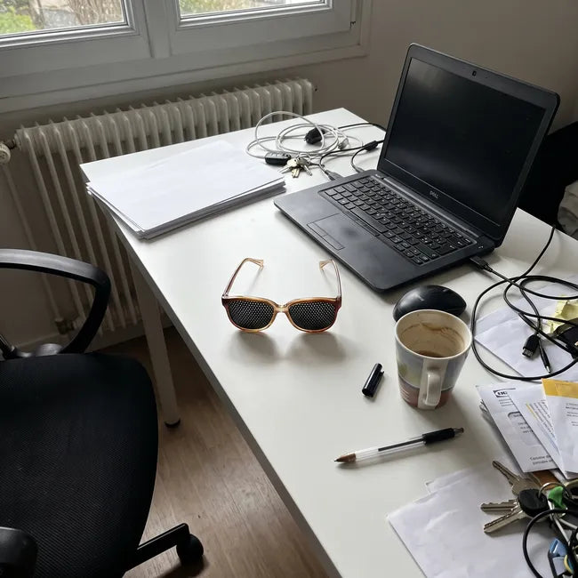 Lunettes à trous posées sur un bureau encombré à la maison, entre ordinateur portable, tasse, câbles et clés