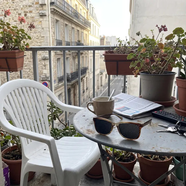 Lunettes à trous posées sur une petite table de balcon avec une tasse de café et un journal